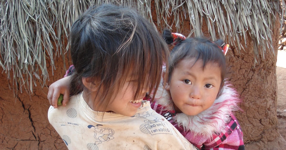 A girl has a small child on her back. The older one is smiling at the younger.