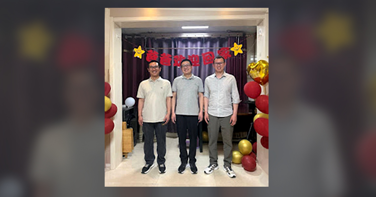 Han Xiaodong (left), Li Jie (center), and Wang Qiang (right) are happily smiling in front of the banner.