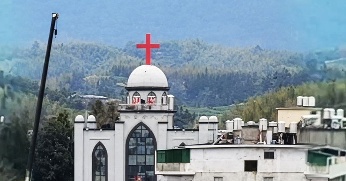A large white church with a brilliant red cross atop is about to be destroyed as seen by the the wrecking ball on the left side of the image.