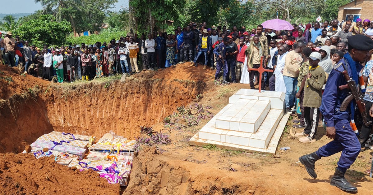 An open grave with many deceased individuals is surrounded by a large group of people.