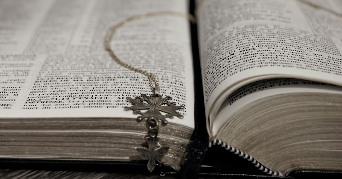 An open Bible holds a metal bookmark with a Coptic cross design. An open Bible holds a metal bookmark with a Coptic cross design.