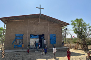 People are entering a small church with a cross on the roof. People are entering a small church with a cross on the roof.