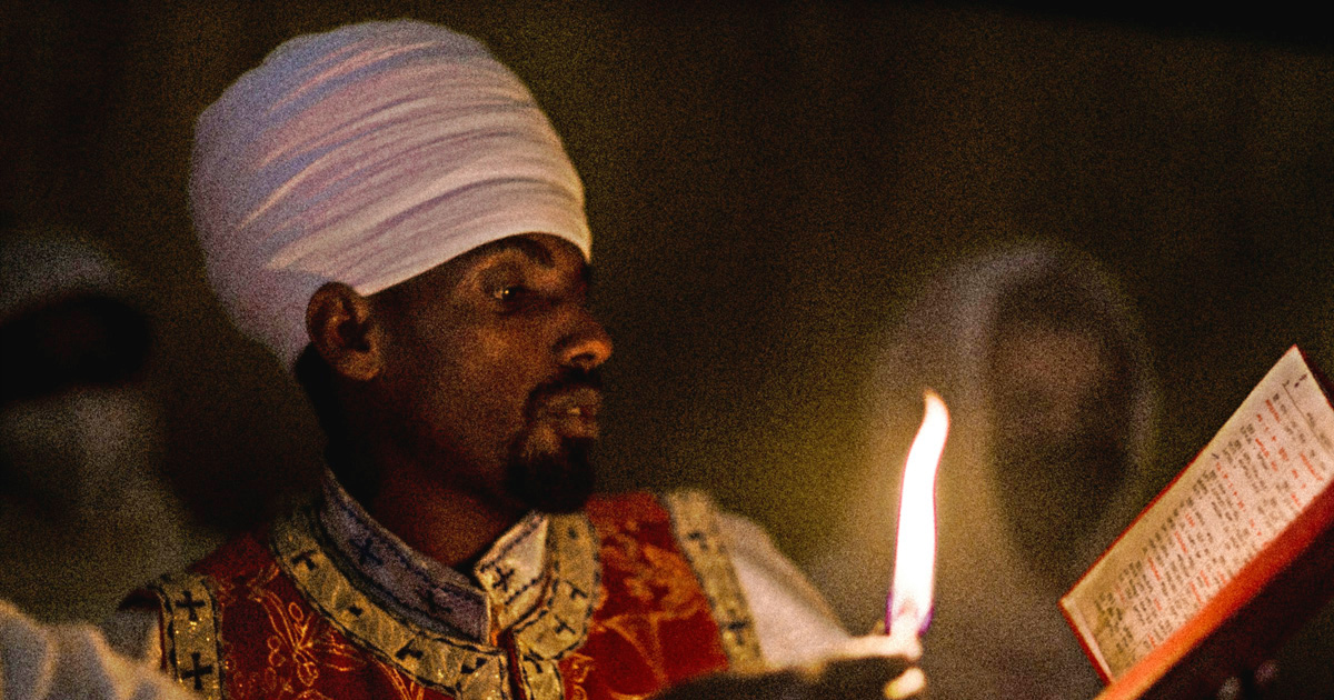Worshippers are illuminated only by candlelight, looking at an open book.