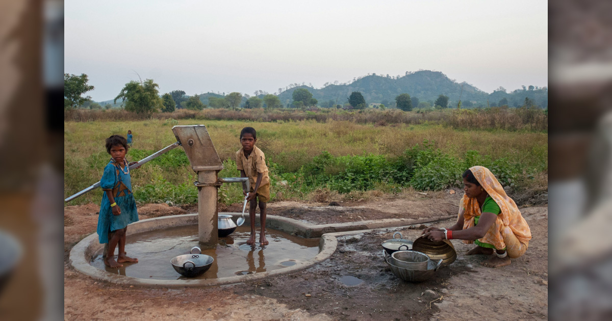 People are gathered at an outdoor water pump.