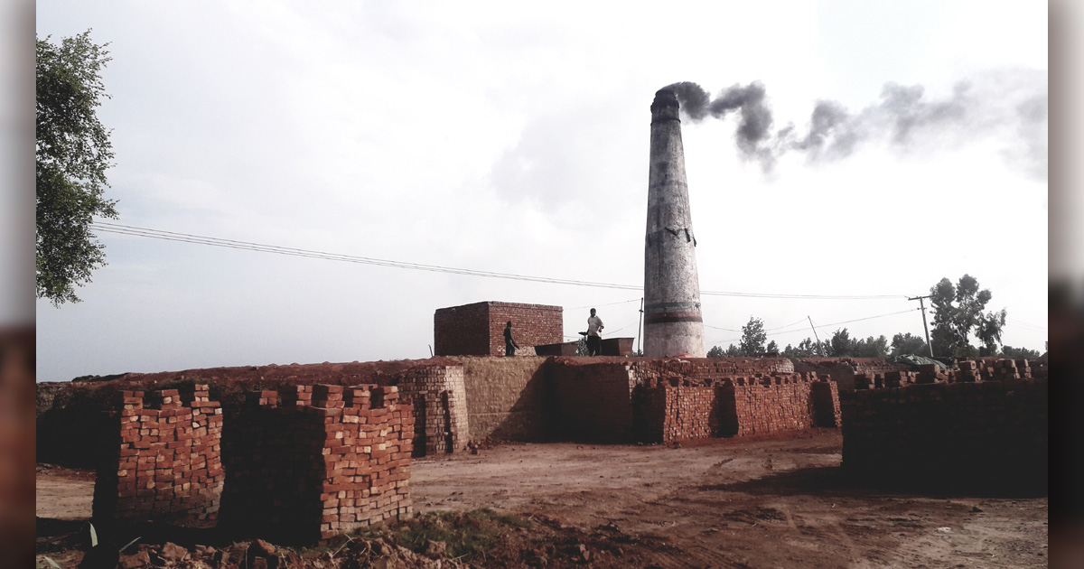 A brick kiln has a very large, smoking chimney which is surrounded by brick buildings. A brick kiln has a very large, smoking chimney which is surrounded by brick buildings.