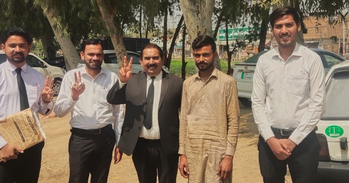 Five men are standing outside. Most are smiling.