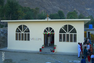 A small church building. A group of people are gathered to one side. A small church building. A group of people are gathered to one side.