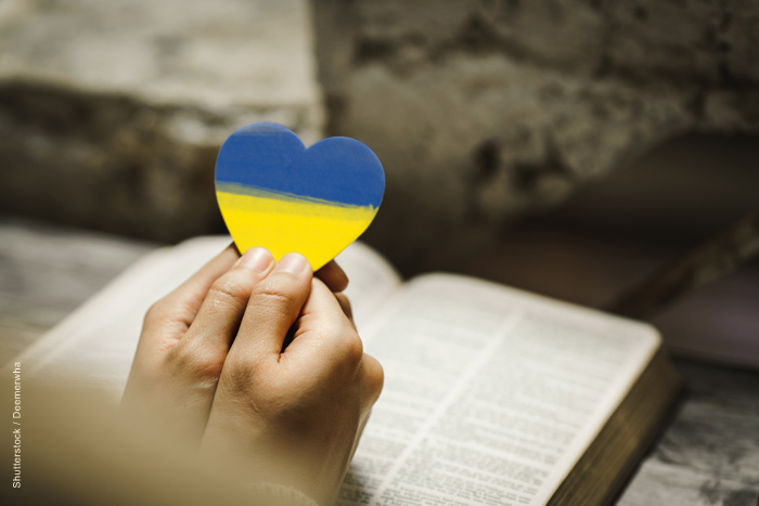 Hands resting on a Bible, holding a blue and yellow heart