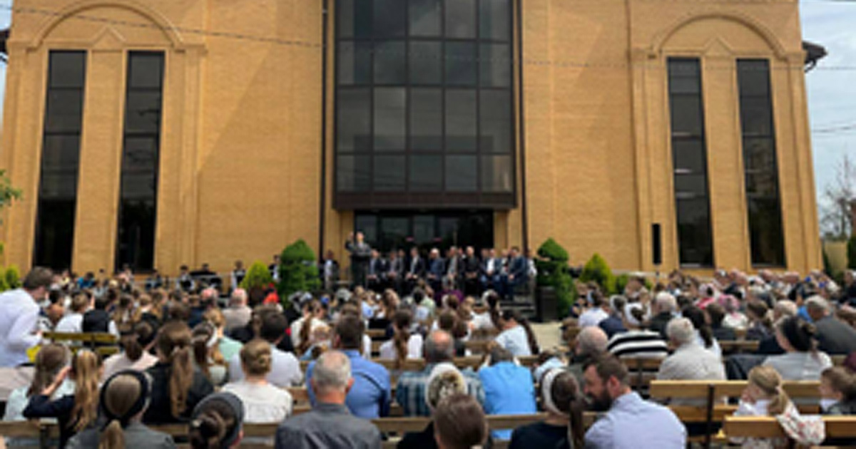 A large congregation meets outside in front of their church.