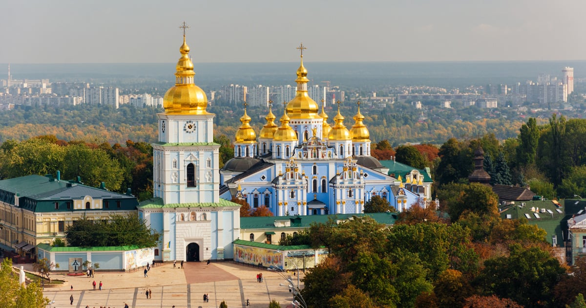 An Orthodox Church of Ukraine monastery is surrounded by trees with a city in the background.