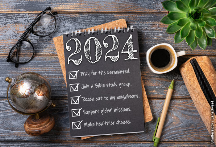A wood desk has a pair of glasses, a small globe, a cup of coffee, and small plant, and a list for 2024 that reads, "Pray for the persecuted, Join a Bible study group, Reach out to my neighbours, Support global missions, and Make healthier choices."