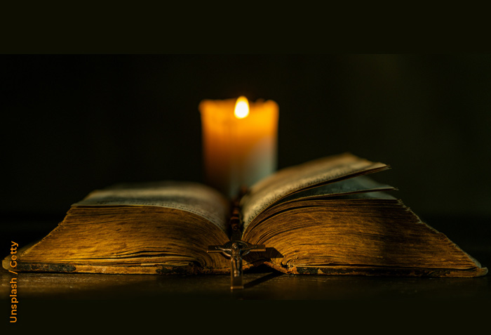 An open Bible is illuminated only by the light of a single candle behind it. An open Bible is illuminated only by the light of a single candle behind it.