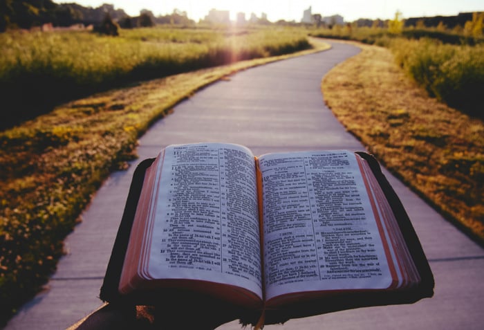 Someone is holding an open Bible while standing on a winding sidewalk.