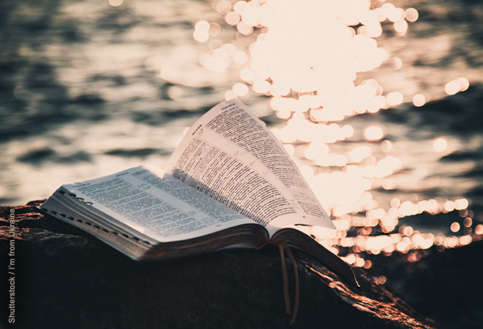 Open Bible on a rock; water with the reflection of the sun in the background Open Bible on a rock; water with the reflection of the sun in the background