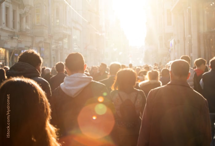 A city street is crowded with people. The buildings around them are almost hidden by brilliant sunlight.