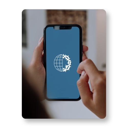 A person is holding a cell phone. The VOMC logo is on the screen. A person is holding a cell phone. The VOMC logo is on the screen.