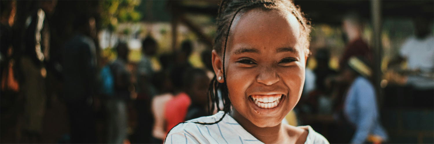 A girl has a big, beautiful smile. There are people in the background.