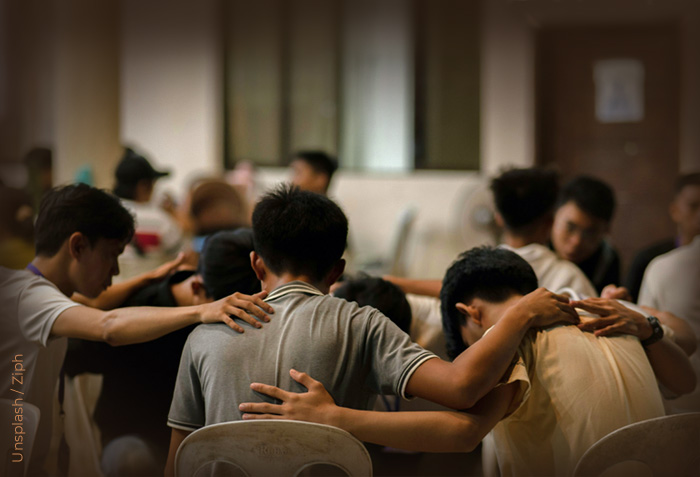 People are praying in small groups with their arms around each other.