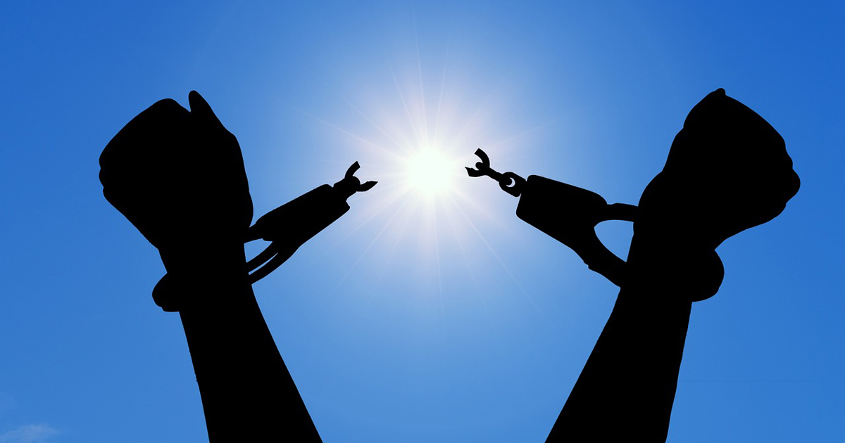 Victorious hands with broken handcuffs are silhouetted against a brilliant sunburst.