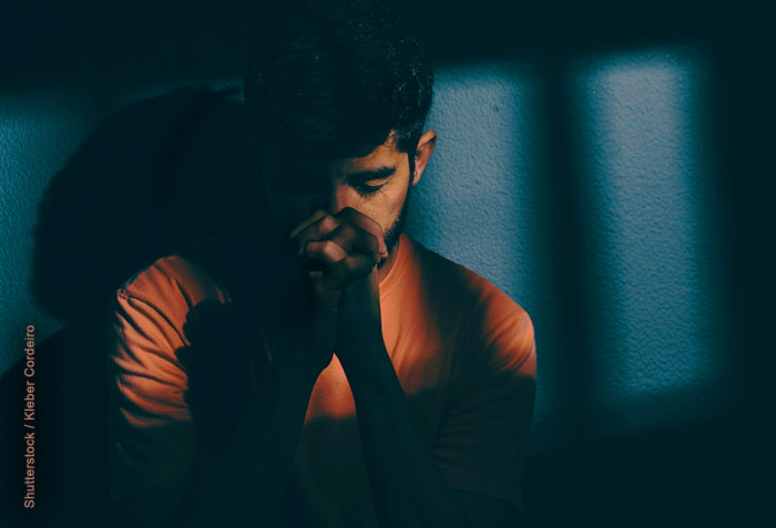 Man praying with shadows of prison bars cast over him