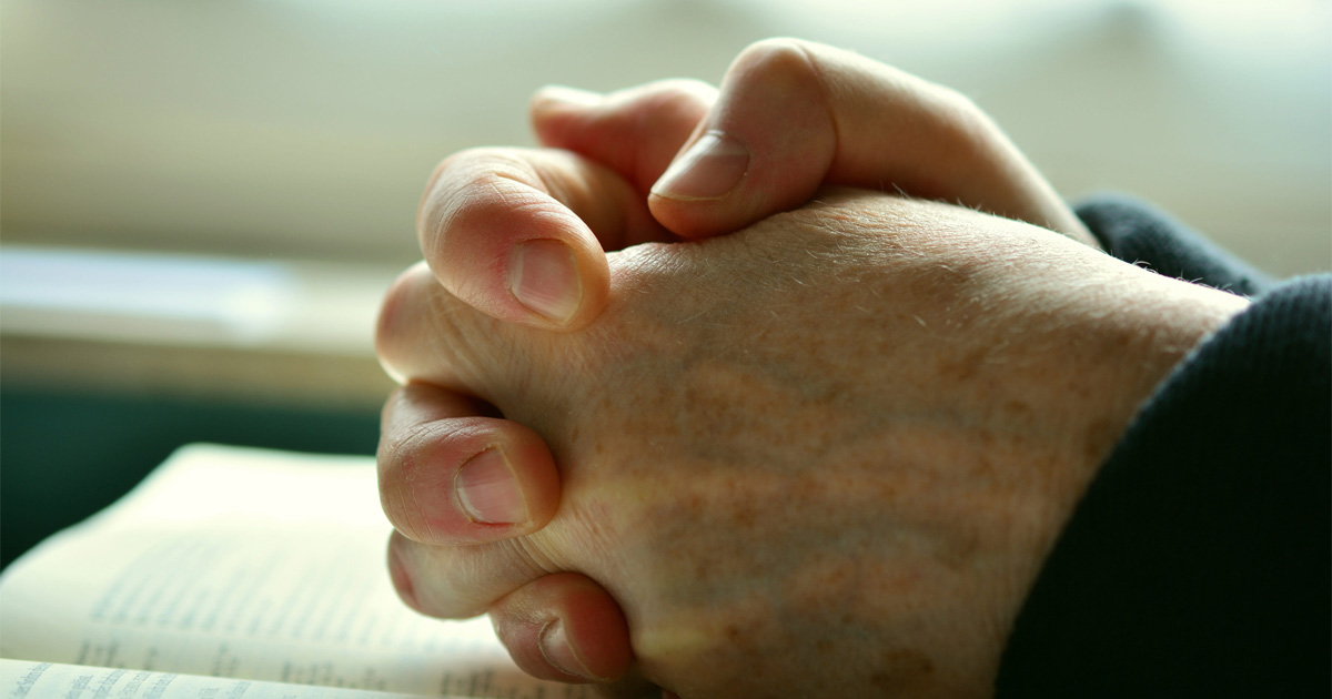 Hands are folded in prayer and resting on a Bible. Hands are folded in prayer and resting on a Bible.