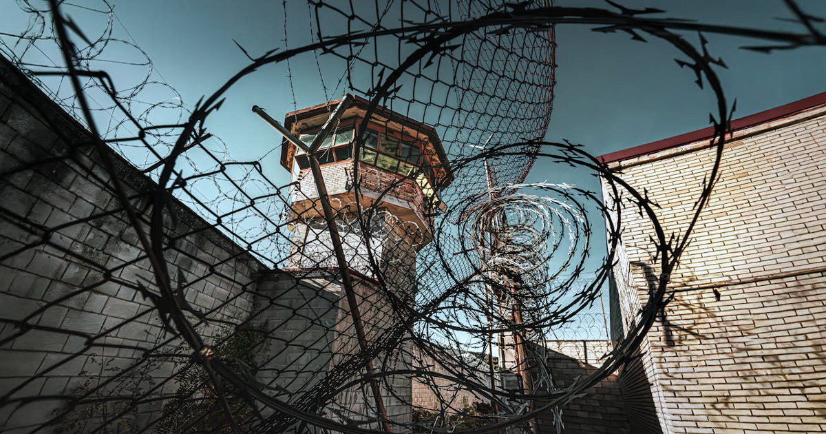 A prison watch tower rises above heavy barbed wire.