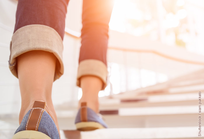 A person is walking up a long flight of stairs. The sun is shining brightly on the second floor.