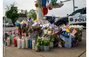 Flowers, candles, and balloons placed as a memorial; police cars behind the display.