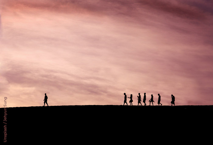 One person is leading a small group of individuals. They are silhouetted against a darkening sky. One person is leading a small group of individuals. They are silhouetted against a darkening sky.