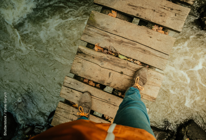 The feet of someone walking across a narrow foot bridge; water is swirling underneath. The feet of someone walking across a narrow foot bridge; water is swirling underneath.
